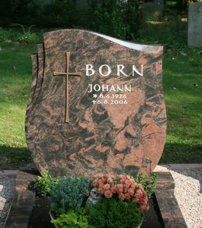 Geschwungenes Grabmal aus rotbraunem Granit mit Bronzekreuz und heller Schrift