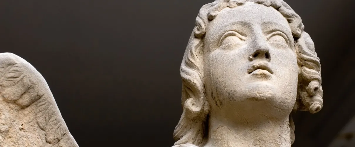 Kopf einer Engelsfigur aus hellem Naturstein vor dunklem Hintergrund